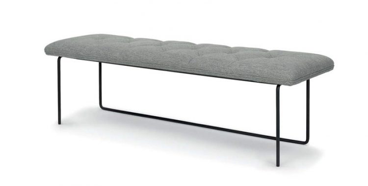 A bench with an intricate leg scheme and a gray cushion.