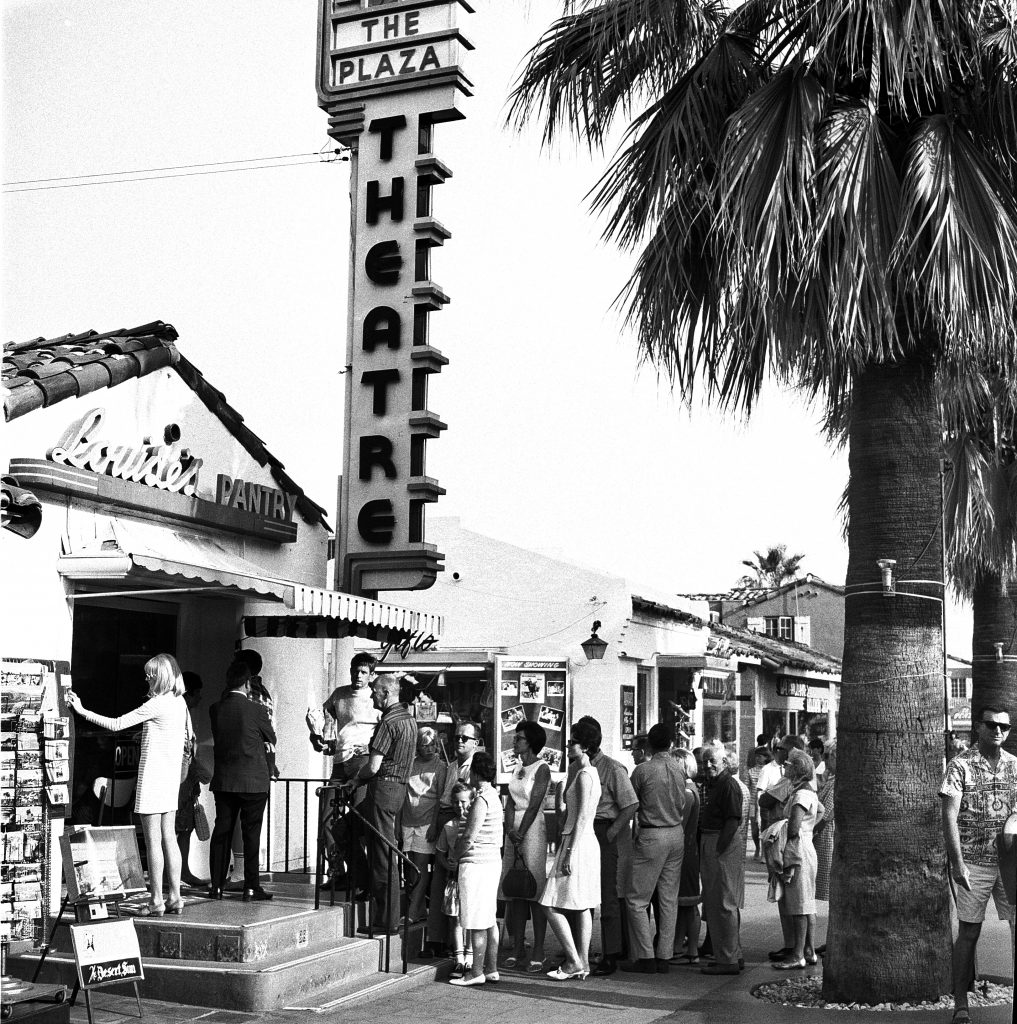 The outside of the Plaza, with a line of people going into a nearby restaurant.