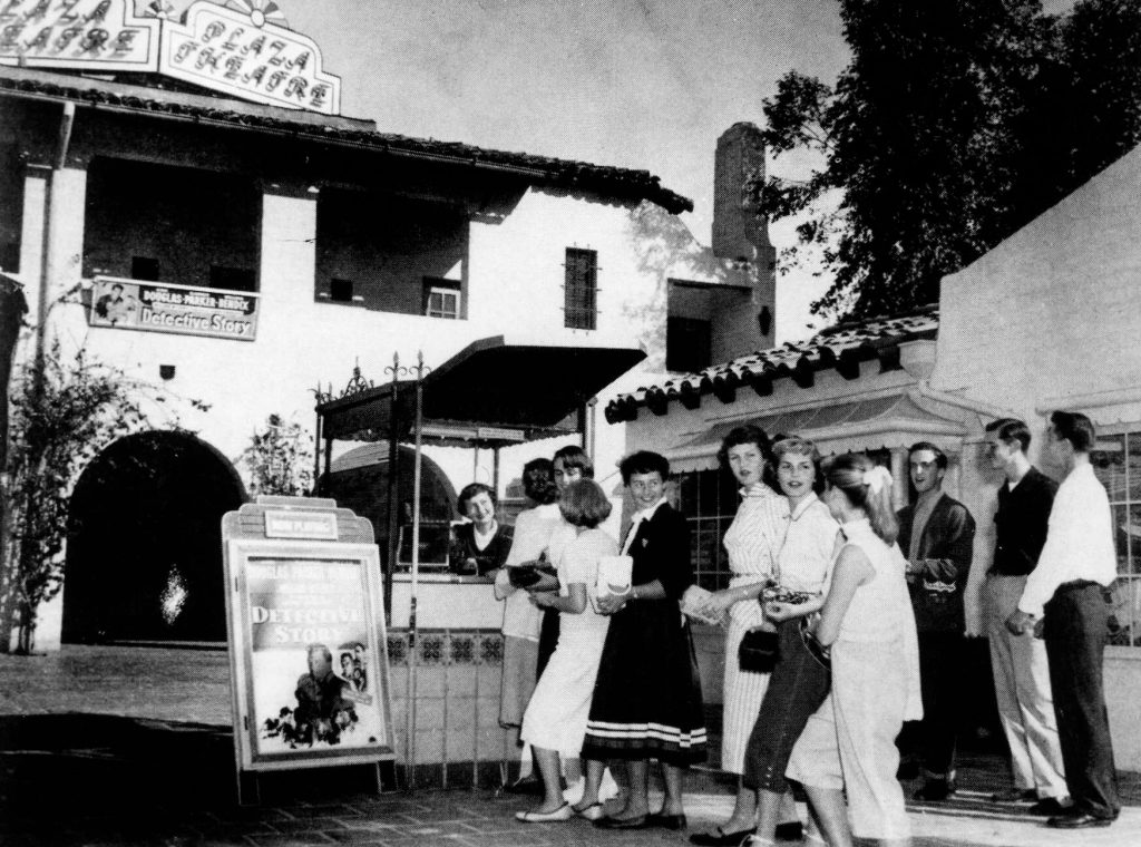 A black and white photograph of people lined up at the plaza theatre looking back toward the camera.