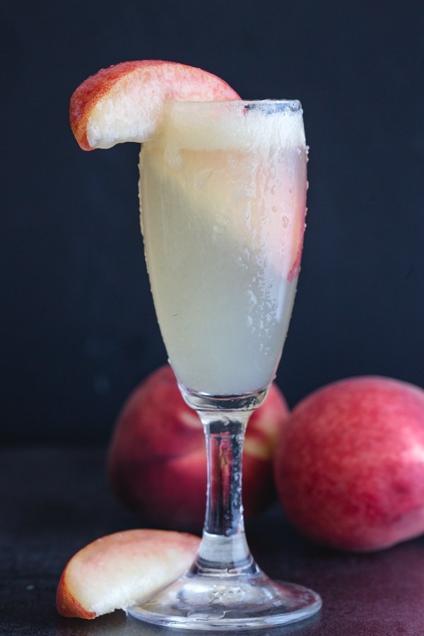 Bellini cocktail in tall clear glass with peach slice