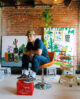 Andrew Cooper, Male, mid 20's artist sitting on chair in painting studio with canvases and art.