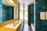 This bathroom features a blue tiled shower, yellow tiled countertops, and a hexagon tiled floor.