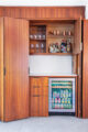 a mini fridge, plus two cabinets that are filled with wine glasses, mugs, and bottles of alcohol