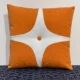 a burnt orange throw pillow with a white starburst design in the middle. 