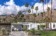 A white Mid Century Modern home exterior with a yellow door and landscaping that includes foliage native to Palm Springs.