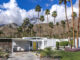 A white Mid Century Modern home exterior with a yellow door and landscaping that includes foliage native to Palm Springs.