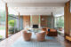 open living room with exposed wood ceiling white Eames lounge chair and floor to ceiling walls of windows