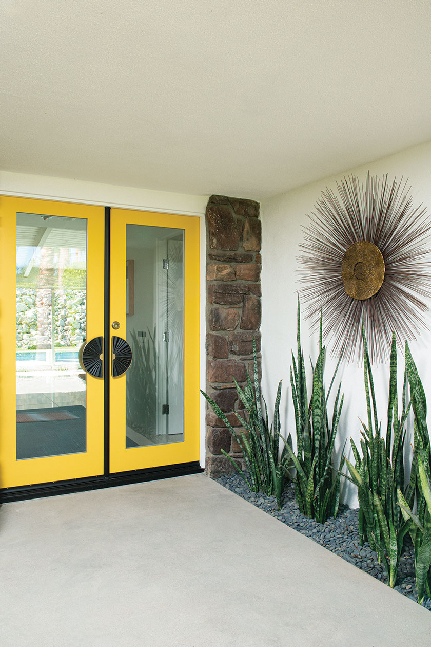 yellow framed front door with large starburst metal sculpture and snake plants in entryway