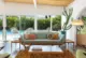 The interior of a Palm Springs vacation rental showing an Adrian Pearsall sofa and a large potted cactus to the right of floor to ceiling windows. The view outside is of the pool and a wall of green hedges. 