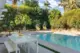 The backyard with features a big rectangluar pool. There are two hanging cage chairs at the far end and a small white minimalistic modern outdoor dining table on the left side foreground. 