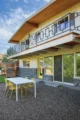 A view of the back of a mid century modern home in Boise with a second story deck bearing a decorative iron railing. On the bottom floor is a gravel patio with a small dining table and chairs.