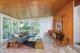A living room with a wood plank ceiling and two walls of floor-to-ceiling windows. Brightly speckled terazzo flooring, a color-blocked geometric rug and modern furnishings are characteristic of a mid century modern home like this one.
