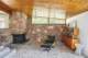 A living room with an slightly angled ceiling made of wood planks. A corner fireplace made of stone is in the background and there is mid century modern furniture in the room. The living room is a sunken down by two steps.