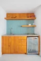 a small counter with a sink and a small wine fridge below the counter. The cabinets are all a wood maple and the backsplash is made of turquoise blue tile.