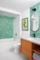 A bathroom with seagreen colored tile in the shower-bath and behind the oval-shaped vanity mirror.