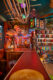 a tiki bar with a red linoluwm counter, a wall of tiki mugs displayed on floor to ceiling shelves on the left side and various tiki collectibles hanging from the walls and ceilings