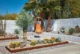Mid-century modern desert courtyard featuring a vintage white metal hanging egg chair with orange and retro-print cushions, centered on a concrete pad surrounded by Corten steel-edged gravel planting beds filled with barrel cacti, succulents, and a sculptural yucca, with tall fan palms rising behind a white block wall under a clear blue sky