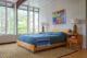 a heywood wakefield bed in a mid century modern room with blue bedding and colorful art above the headboard
