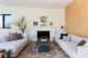 Malibu mid century living room with two white linen sofas facing each other over a vintage Persian rug and a matte black square coffee table, centered on a fluted white marble fireplace with a small gallery wall above, flanked by a tall branch arrangement and a warm oak panel accent wall