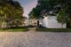 Twilight exterior of a single-story modern home with white vertical-paneled siding and flat roofline, illuminated from within, framed by mature trees and a landscaped stone walkway leading to the front door