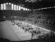 a large hangar-style hall filled with rows of table tennis tables and players