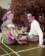 A man and a woman sitting on a ping pong table and holding paddles