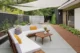 Covered backyard patio of a Victor Hosfrod home with built-in seating, outdoor coffee table, concrete paving, garden beds and a large shade sail.