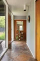 Long interior hallway with original wood paneling, stone or tile flooring, large windows and a view toward a furnished room at the far end.