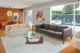 Mid-Century Modern living room with a white sofa, dark gray sectional, round coffee table, patterned rug, wood-paneled wall and large corner windows.