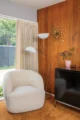 Living room corner with a cream lounge chair, white globe floor lamps, mahogany wall paneling, a dark wood cabinet and large window.