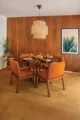 Mid-Century Modern dining room with an oval wood table, orange upholstered chairs, pendant light, mahogany-paneled wall and framed artwork.