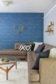 Seating area with a gray sofa and blue accent pillows against geometric blue wallpaper, paired with a cream armchair and wood coffee table.