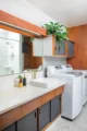 Primary bathroom and laundry area with white countertop, wood-and-gray cabinetry, vessel sinks, open shelves and a washer and dryer.