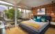 Mid-Century Modern bedroom with a gray upholstered bed, colorful blue and yellow pillows, wood accent wall and large glass doors opening to a patio.