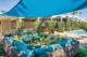 Palm Springs outdoor lounge with turquoise and yellow seating arranged around a glass coffee table beneath a blue shade sail.