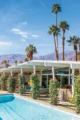 Mid-Century Modern Palm Springs home with a white flat roof, swimming pool, tall palm trees and mountain views.