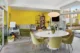 Mid-Century Modern living and dining area with a bright yellow wall, round dining table, olive chairs, white sofa and large glass doors.