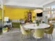 Mid-Century Modern living and dining area with a bright yellow wall, round dining table, olive chairs, white sofa and large glass doors.