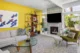 Mid-Century Modern living room with a yellow accent wall, gray sofa, olive lounge chair, wood shelving and white tiled fireplace.