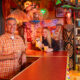 a man and woman in a tiki room bar with tiki drinks in hand